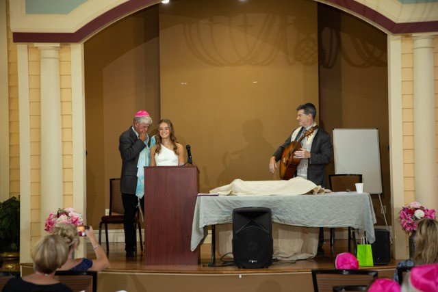 A young girl receives a shawl during her Bat Mitzvah ceremony, as Rabbi Cantor Ron Broden stands by in a synagogue.